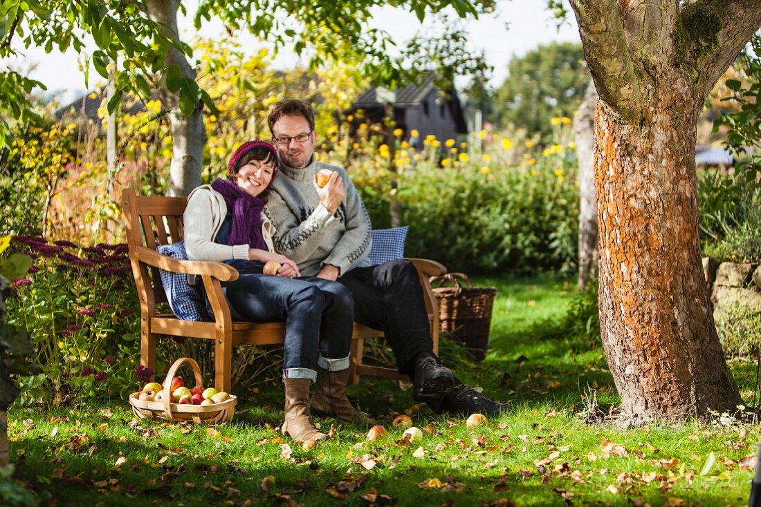 Woman and man sitting on garden bench in sunny garden with fresh apple harvest