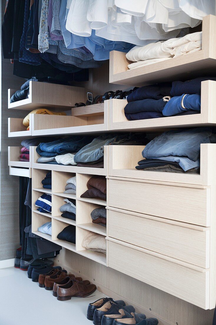Open-fronted wardrobe with clothing hung from rail and drawers in dressing room