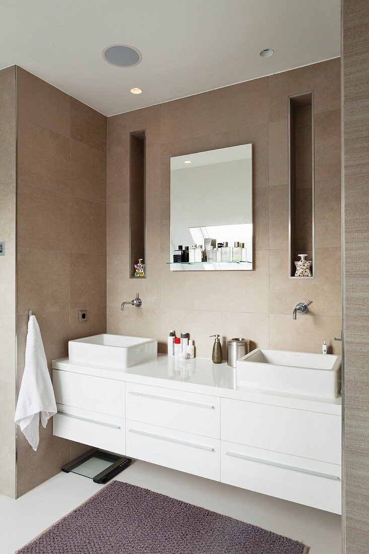 White washstand with twin countertop basins built into niche in tiled wall