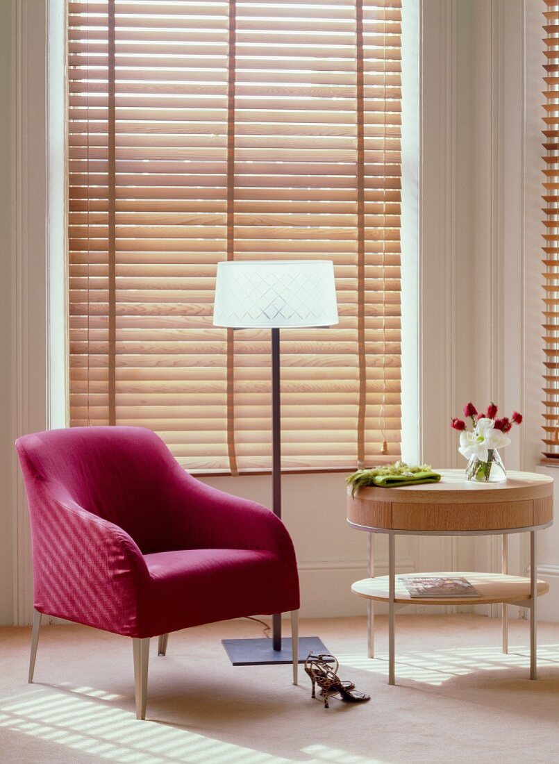 Magenta armchair, modern, elegant standard lamp and small, designer table in front of wooden louvre blinds on bay window