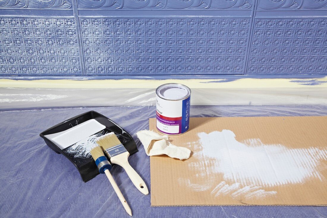 Painting utensils on floor in front of wall covered in Lincrusta (structured linoleum wallpaper) painted blue