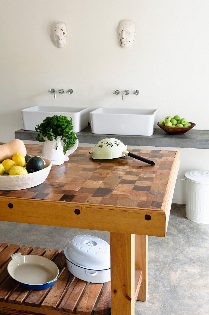 Kitchen table with cross-grained mosaic surface in front of sink unit with two countertop basins in minimalist kitchen