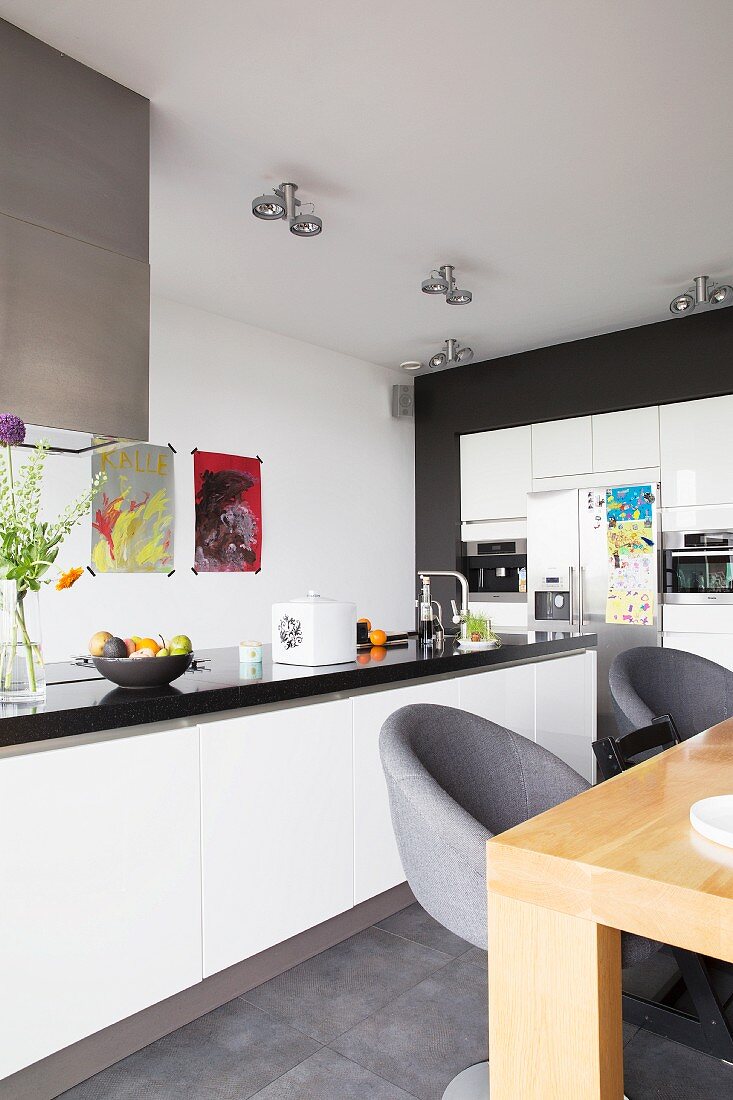 Swivel chairs with grey upholstery at wooden table and free-standing counter with white base units in contemporary kitchen