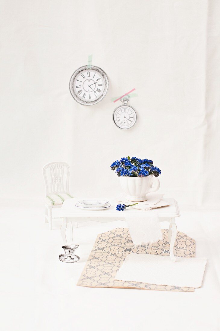 Forget-me-nots in teacup and dolls'-house furnishings with tiny clocks on wall