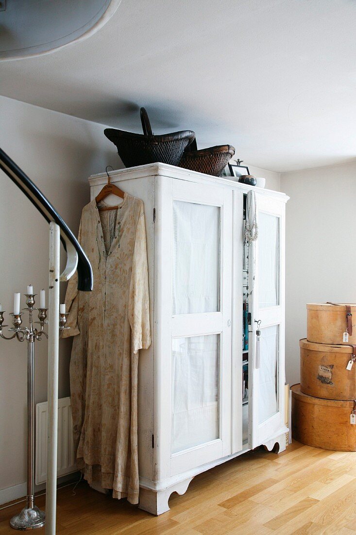 Long dress on coat hanger hung on white-painted wardrobe with dark baskets on top