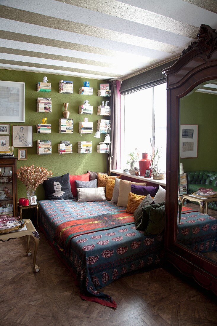 Tagesbett mit vielen Kissen im Wohnzimmer mit grüner Wand und grün-weißem Streifenmuster an der Decke