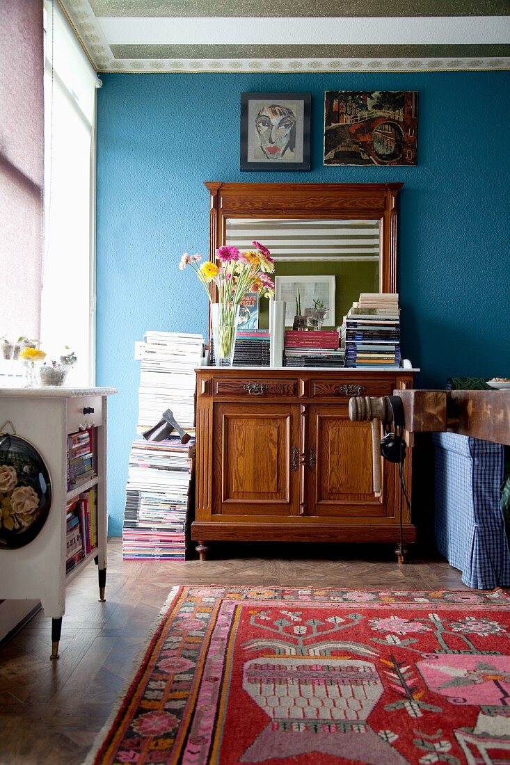 Antike Spiegelkommode vor blauer Wand mit Zeitschriftenstapel