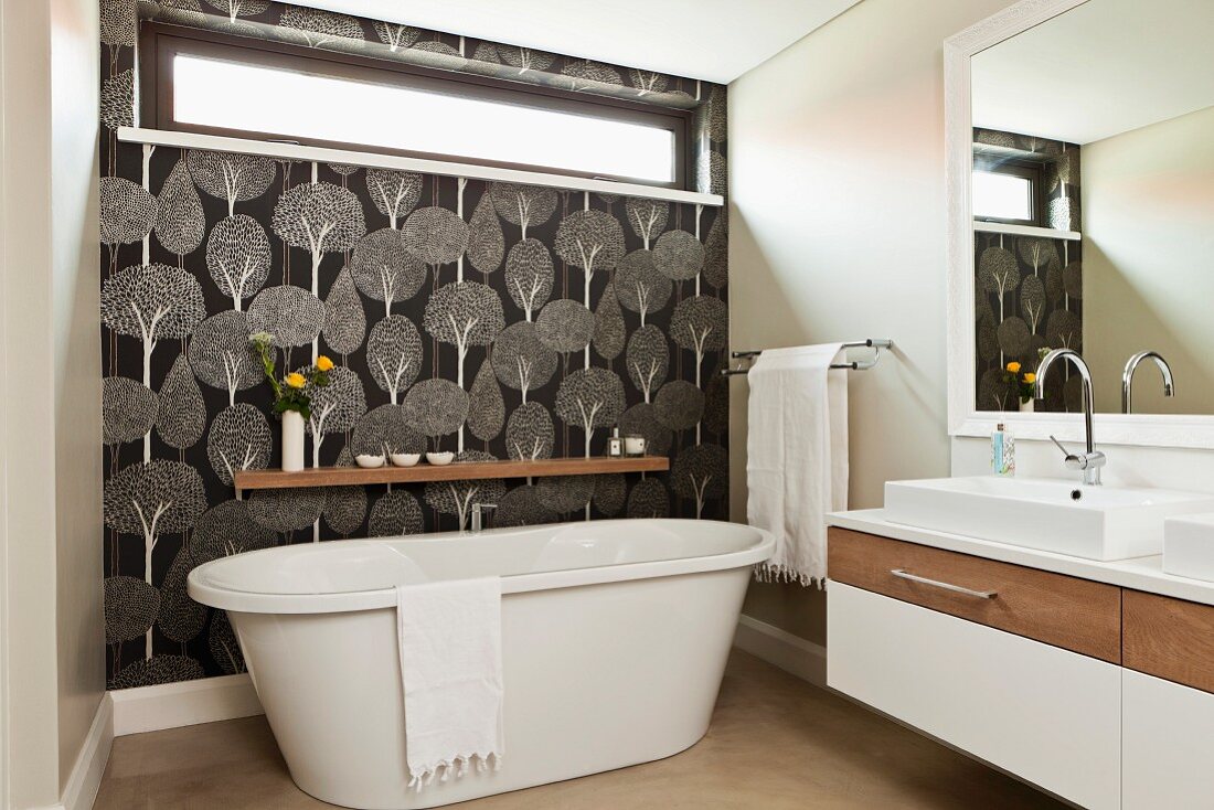 Freistehende Badewanne vor Wand mit Oberlicht-Fenster und schwarz-weißer Tapete mit Baummuster in Designerbad
