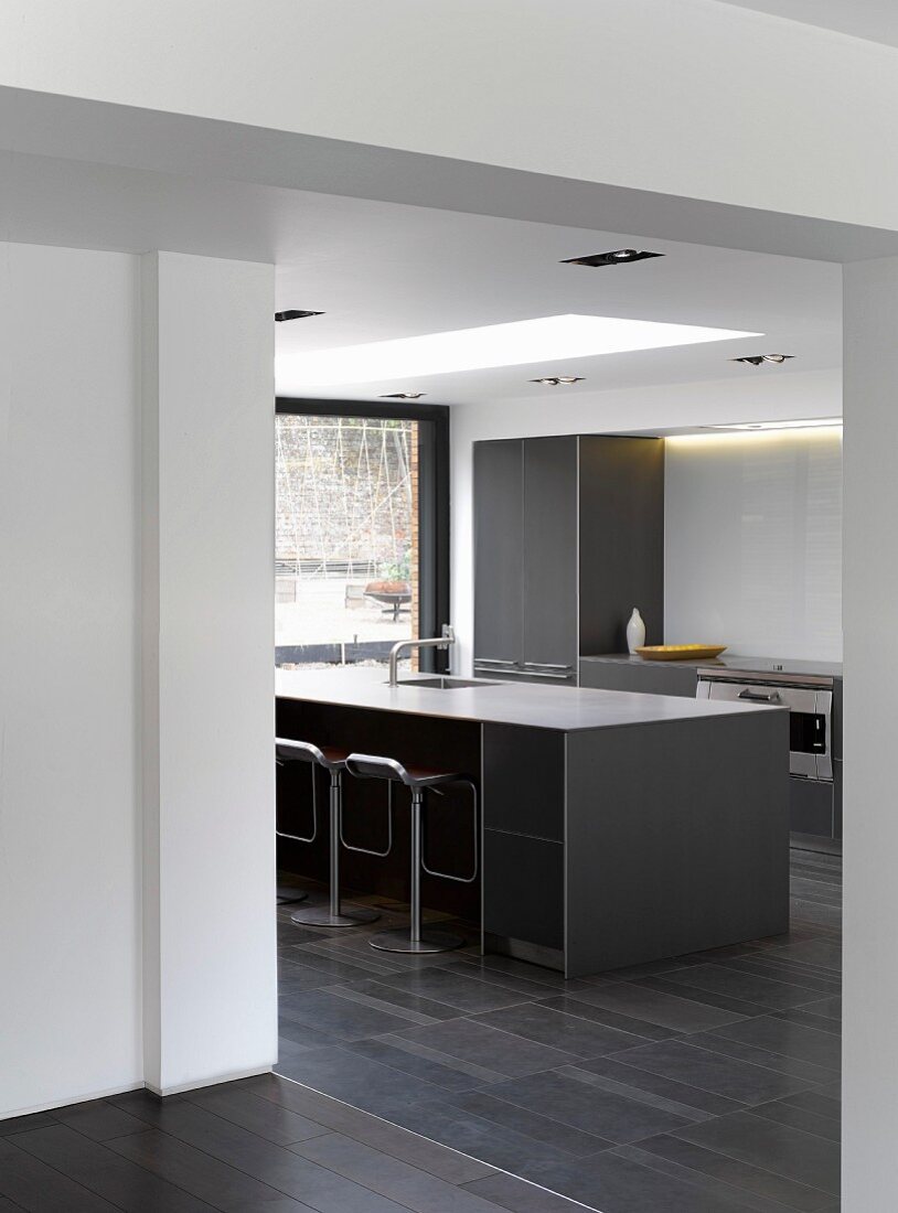 Blick vom Vorraum in Küche, Barhocker vor grauem, monolithischem Küchenblock in zeitgenössischem Wohnhaus