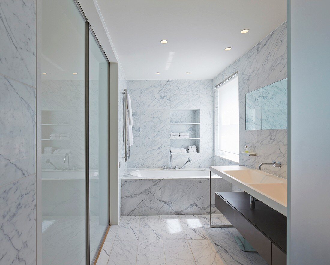 Edles Marmorbad, seitlich minimalistischer Waschtisch, vor Badewanne am Fenster