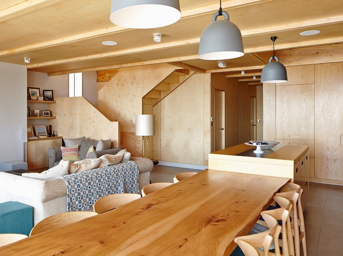 Lange Esstafel aus Massivholz, darüber Designer Hängeleuchten mit Retroflair an Holzdecke in offenem Wohnraum
