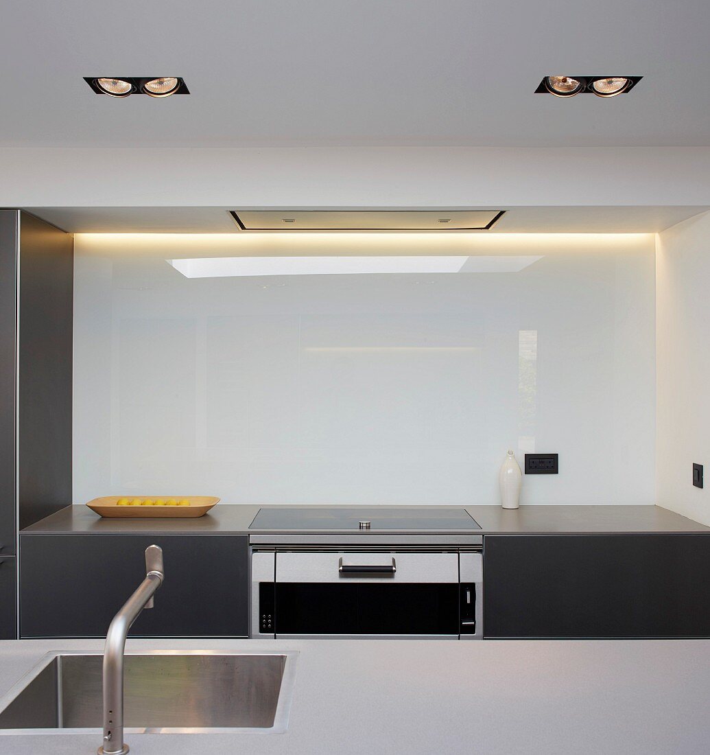 Blick über Küchentheke mit eingebautem Spülbecken auf Küchenzeile in Nische mit beleuchteter Glaswand