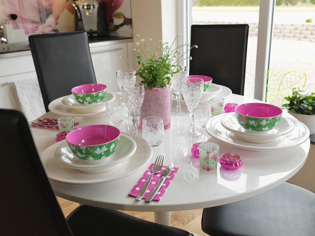 Place settings with colourful bowls on round table with black, leather-covered chairs