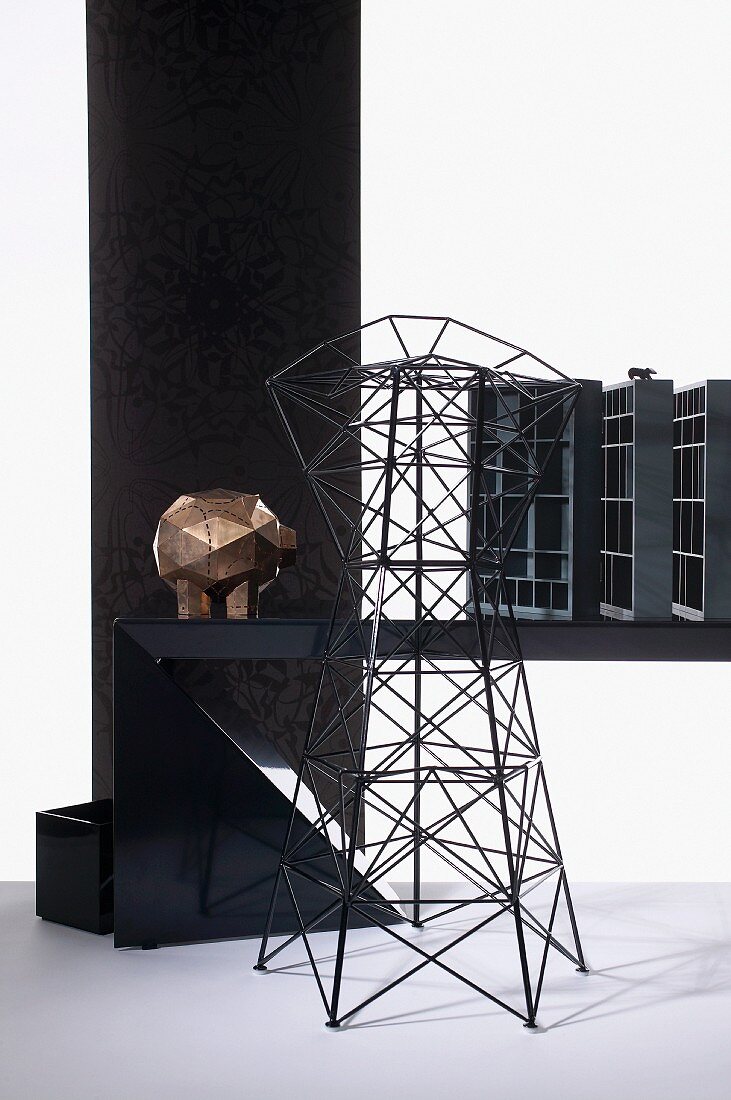 Turm aus Metalldraht vor einer Schwein-Skulptur auf Tisch mit Setzkästen, dahinter eine schwarze Wand mit Prägemuster