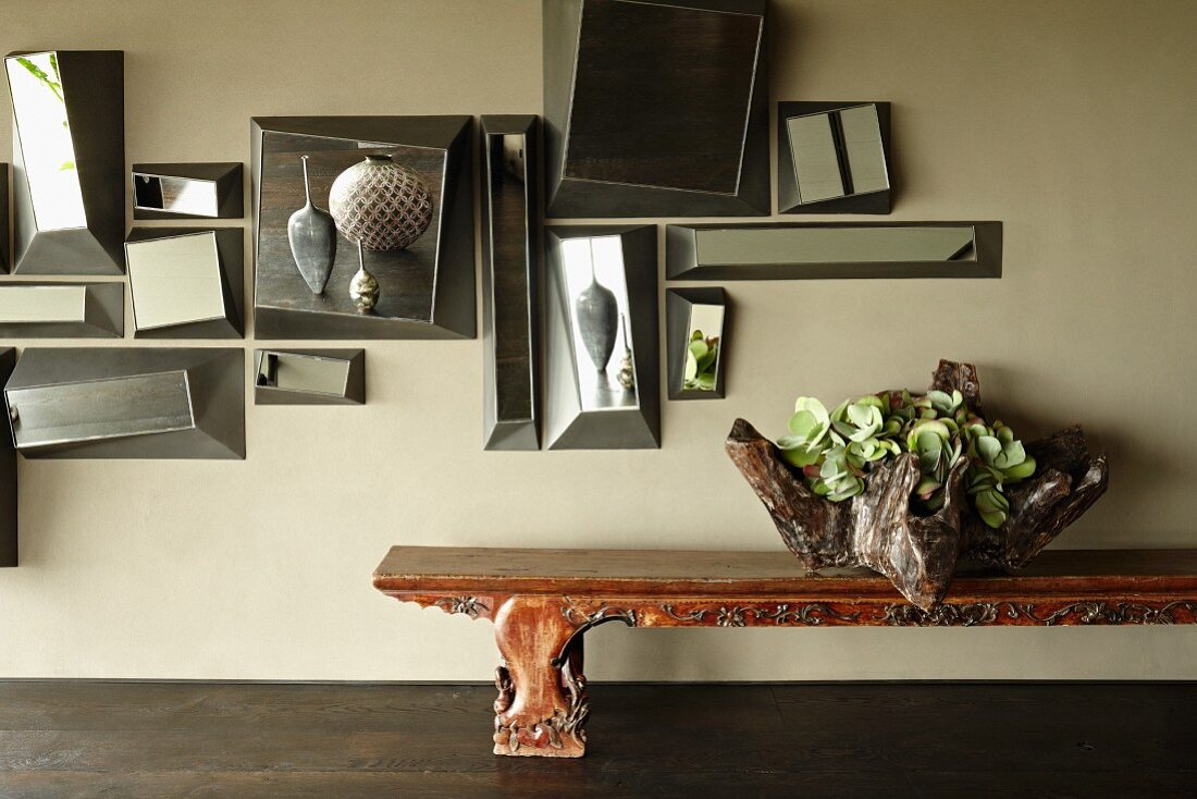 Collage of mirrors on wall above wooden bench decorated with sculptural bowl