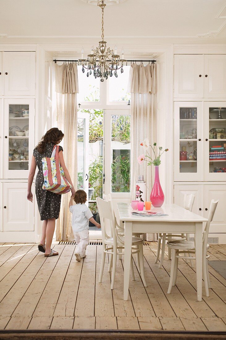 White dining room in country-house style; mother and toddler in background