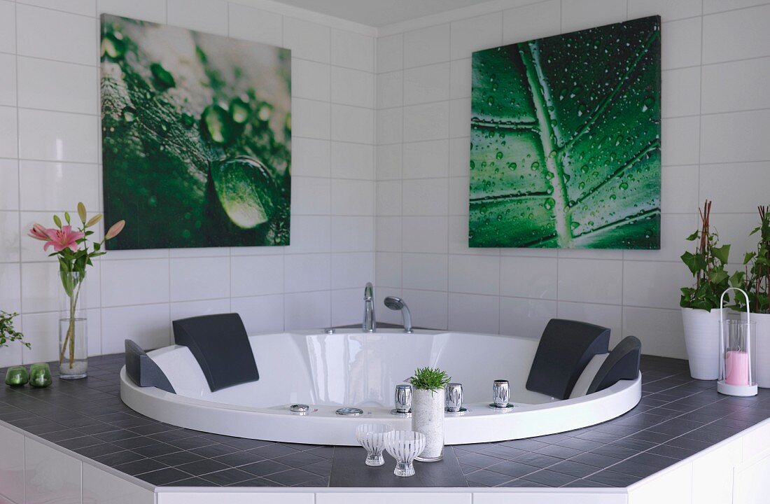 Whirlpool tub in white-tiled bathroom below pictures with leaf motifs on wall