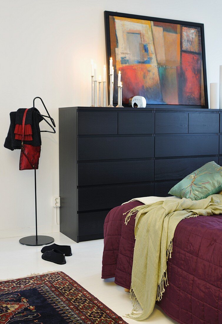 Partially visible bed, black chest of drawers and modern valet stand