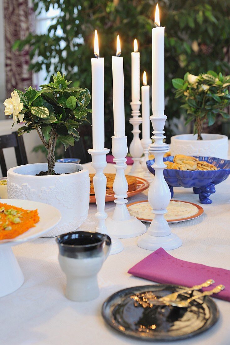 Lit candles in white candlesticks on set table