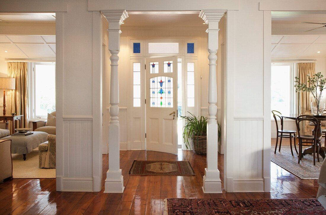 Blick vom Foyer in Hauseingang mit weissen Holzsäulen und Haustür mit bunten Gläsern, teilweise sichtbarer Wohn- und Essbereich in elegantem renoviertem Cottage