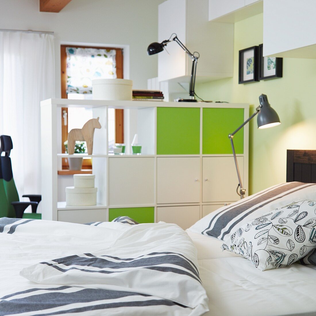 A view from a bed of a room divider with closed elements in white and friendly green with retro-style lamps and bed clothes