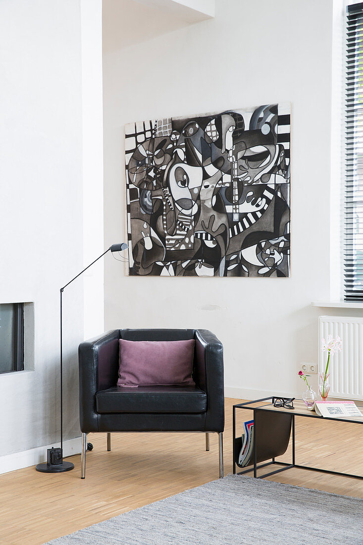 Black leather armchair and standard lamp below black and white modern artwork in corner