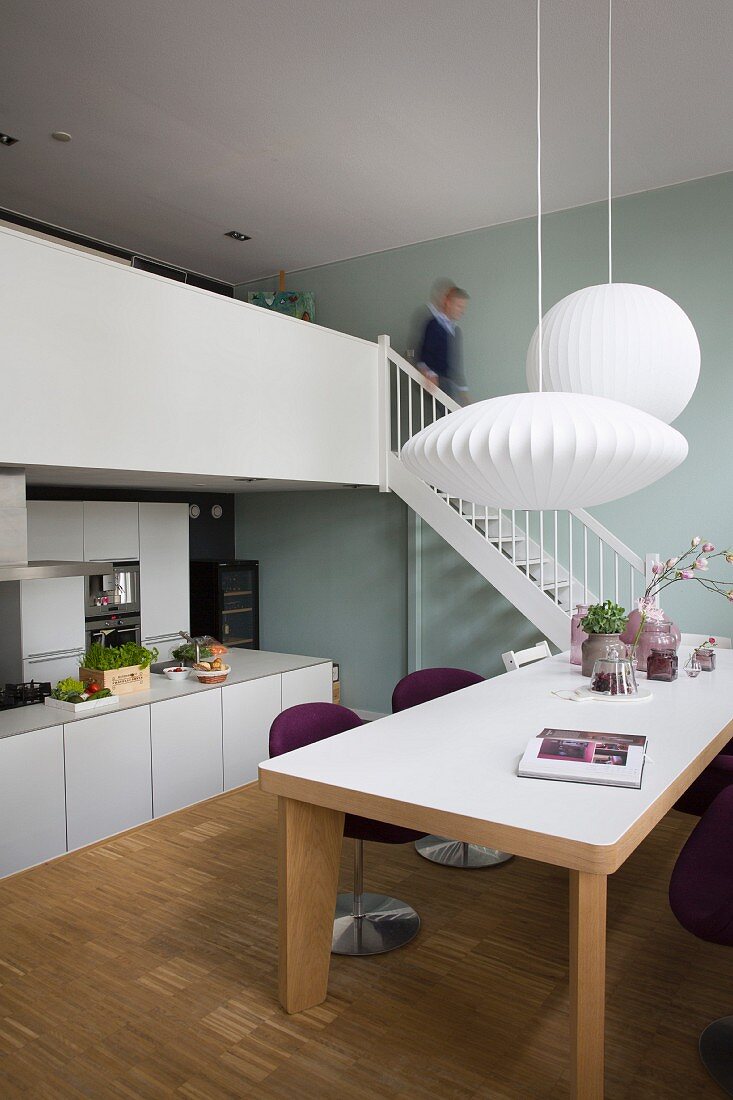 Dining area with modern table below white pendant lamps and free-standing kitchen counter below gallery