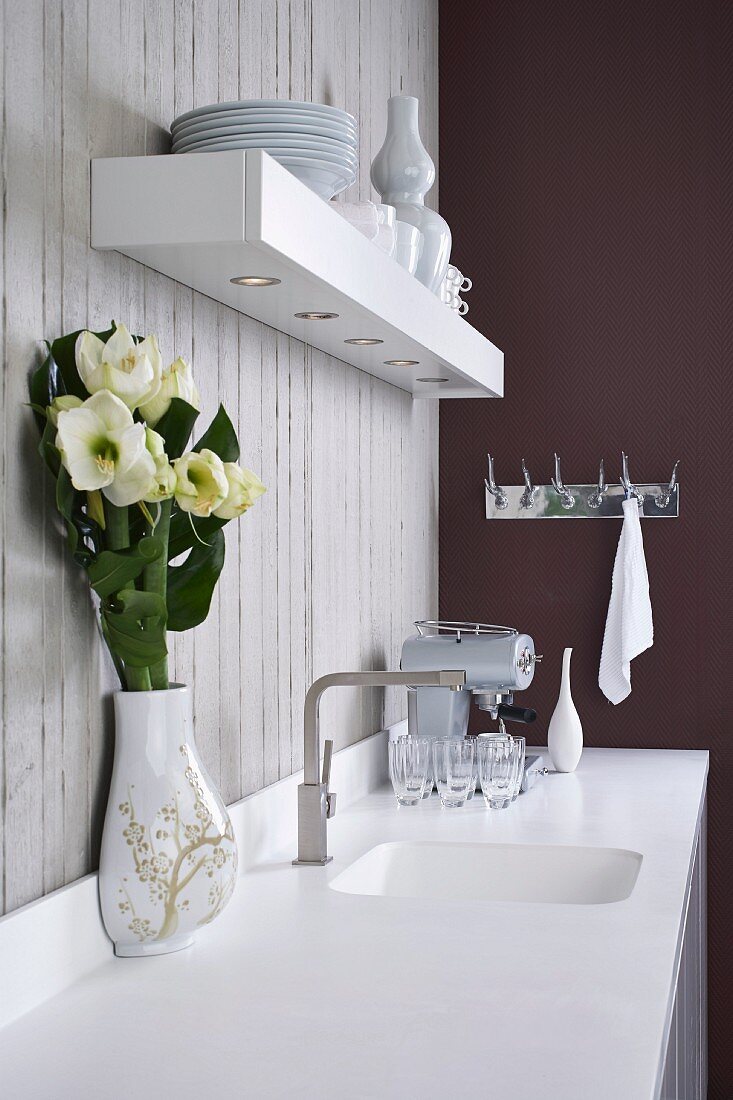 Corian Arbeitsfläche mit integriertem Spülbecken und Wandbord mit Downlights vor Sichtbetonwand in minimalistischer Designerküche