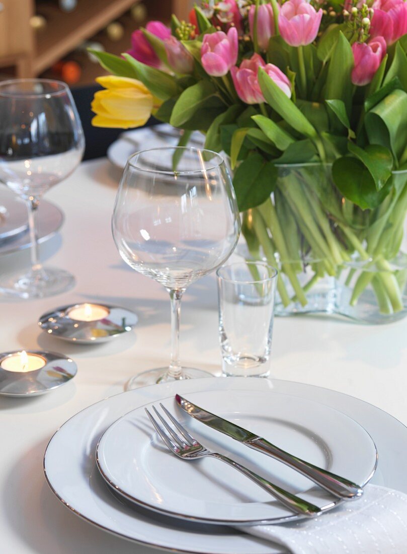 Weisses Gedeck mit Weingläsern, Teelichter neben Tulpenstrauss in Glasvase