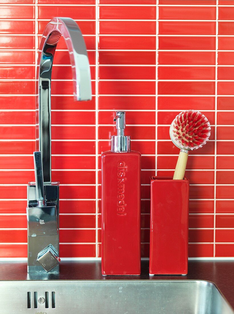 Seifenspender aus Keramik und Küchenbürste auf Edelstahlspüle mit moderner kantiger Armatur, rote Mosaikfliesen als Spritzschutz