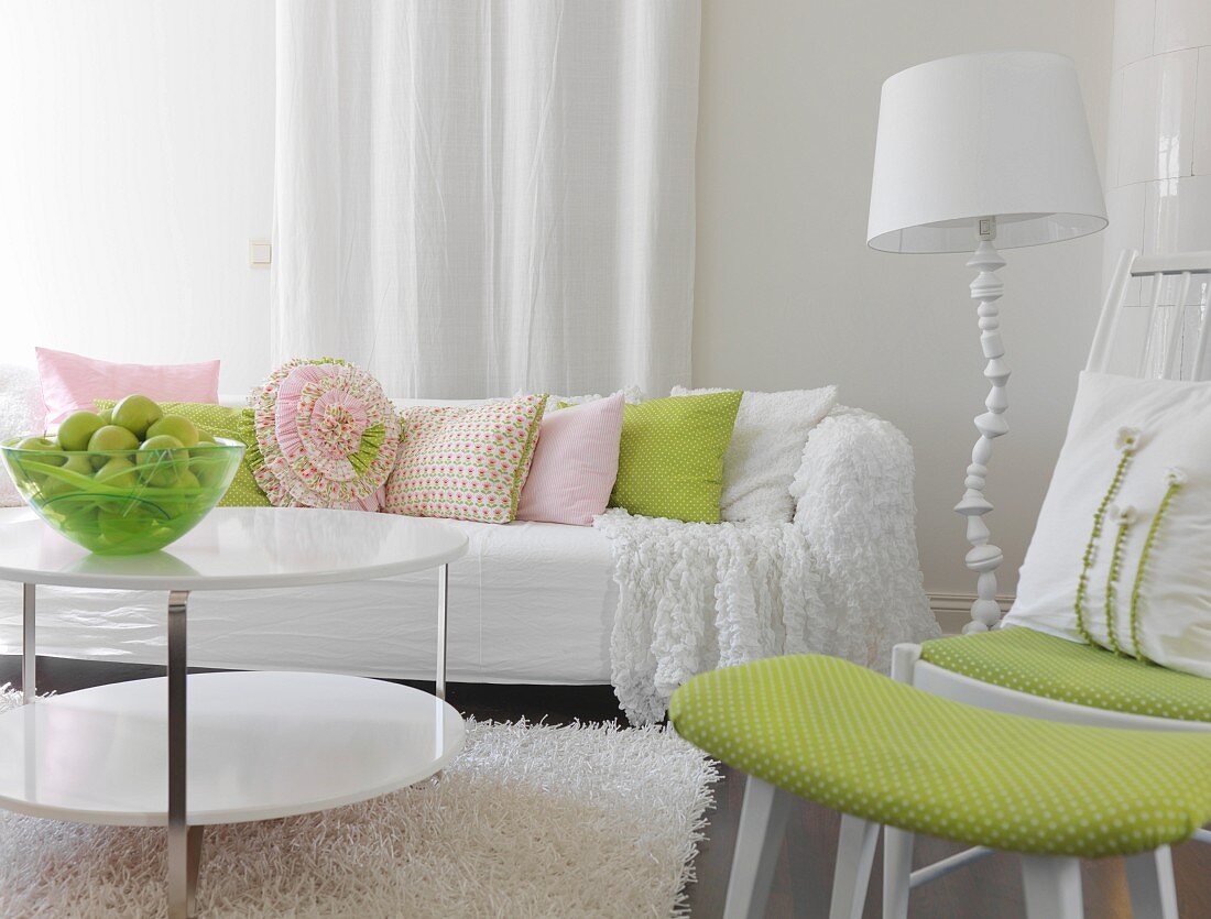 weiße Couch mit pastellfarbenen Kissen, Obstschale auf Couchtisch, seitlich Stuhl mit passendem Fussschemel