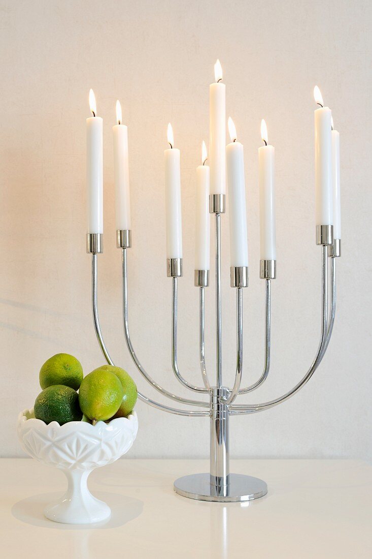Lit, white candles in multi-armed candelabra and small bowl of fruit