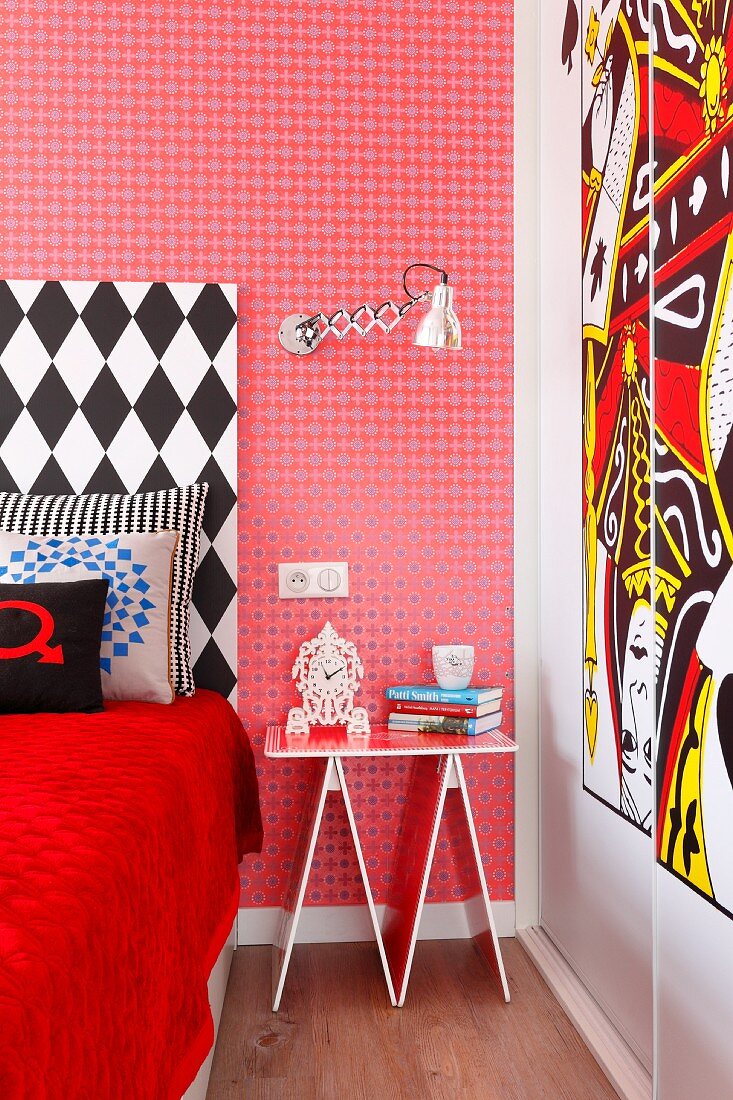 Eklektisches Schlafzimmer mit roter Mustertapete und schwarz-weißem Bettkopfteil, dekoratives Nachttischchen und moderner Kunst