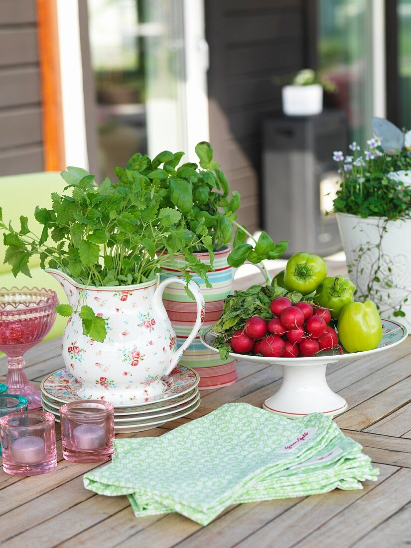 Bowl of vegetables, retro jug of herbs, tealight holders and linen napkins on wooden table