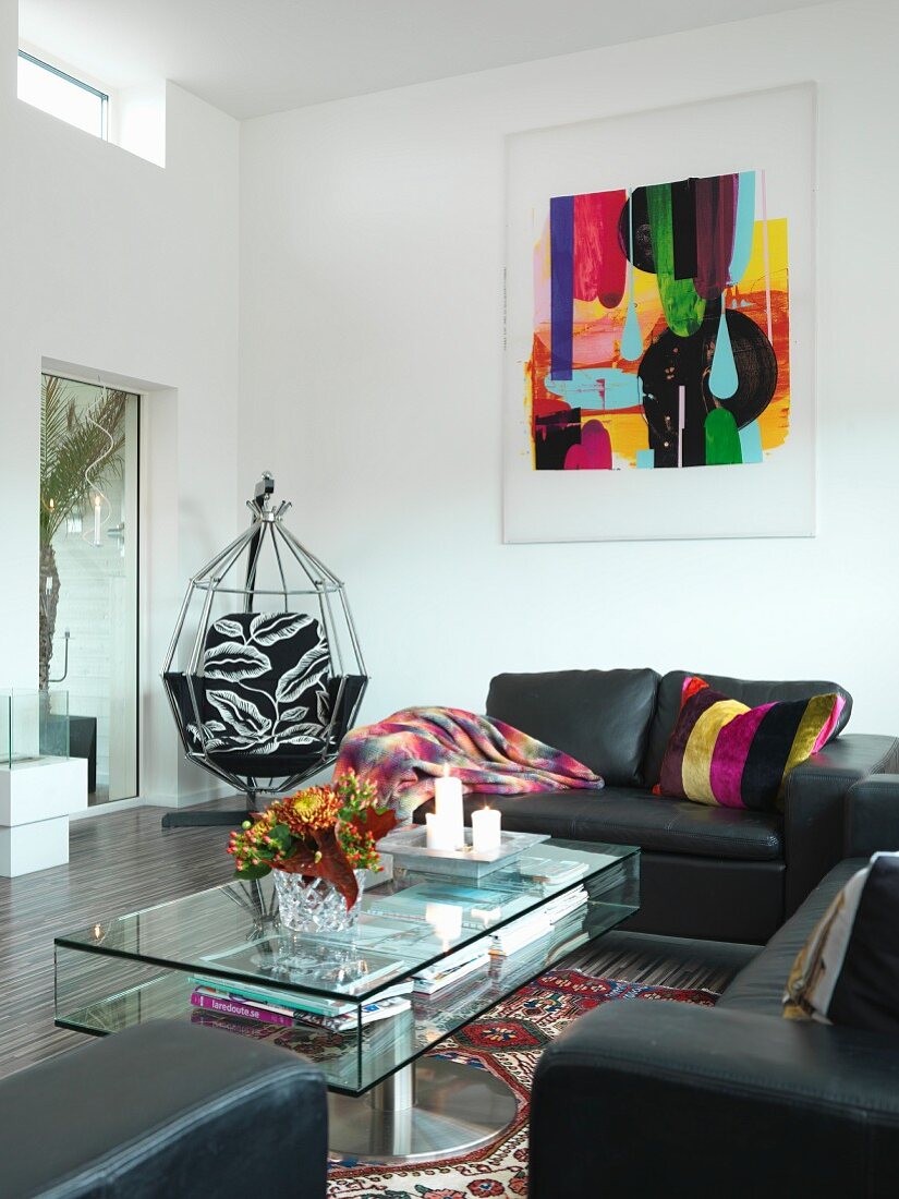 Black leather sofa set and glass coffee table in living room with modern artwork on wall