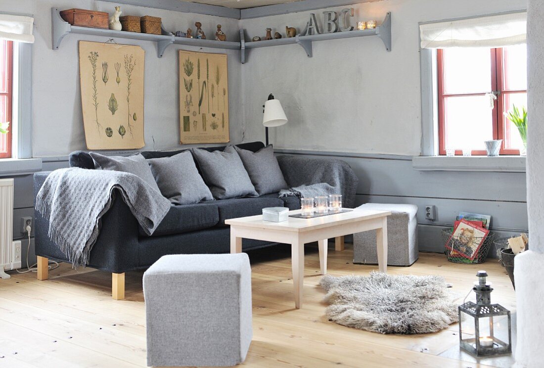 Polsterhocker und graues Sofa um Couchtisch in grau getönter Wohnzimmerecke, auf Dielenboden Tierfell