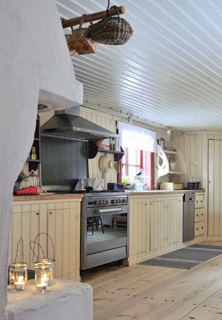 Rustic, cream kitchen counter with stainless steel gas cooker and white, wooden ceiling