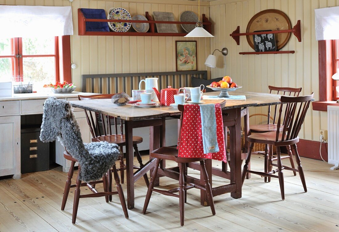 Tassen und Kanne auf Holztisch in rustikaler Zimmerecke mit cremefarbener Holzverkleidung, Teller auf Wandbord