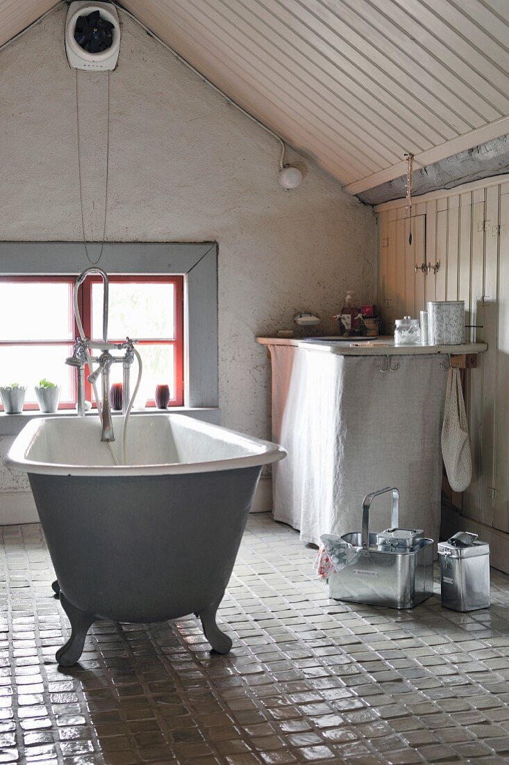 Freistehende Vintage Badewanne auf glasiertem Keramik-Fliesenboden im Bad unter dem Dach, Fenster in Giebelwand
