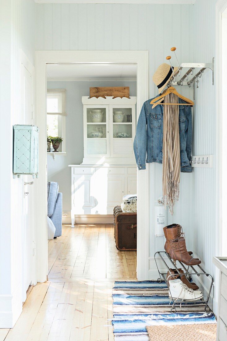 Holzverkleideter Gang in Pastellton mit Garderobe, neben offener Tür und Blick auf Anrichte in ländlichem Ambiente