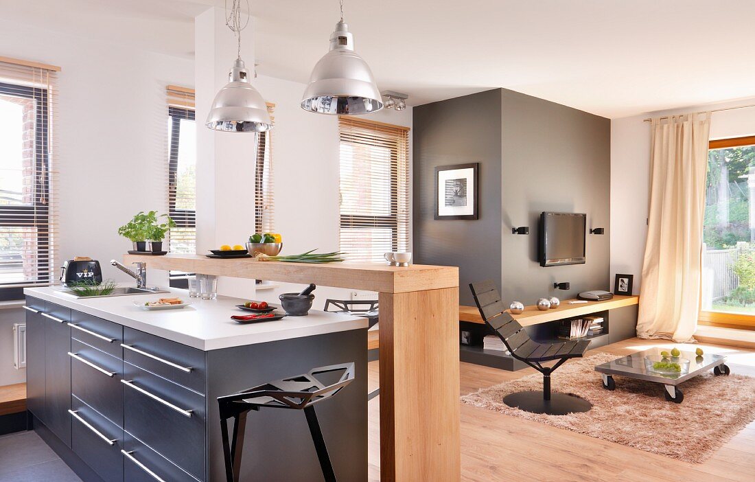 Küche mit Mittelblock und minimalistischer Theke aus Holz, gegenüber Lounge mit Sessel und Bodentisch auf Teppich in modernem, offenem Wohnraum