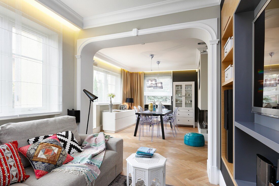 Helle Couch und marokkanische Kissen in Loungebereich, Blick durch breiten Durchgang in Esszimmer, in offenem Wohnraum mit Jugendstil Elementen