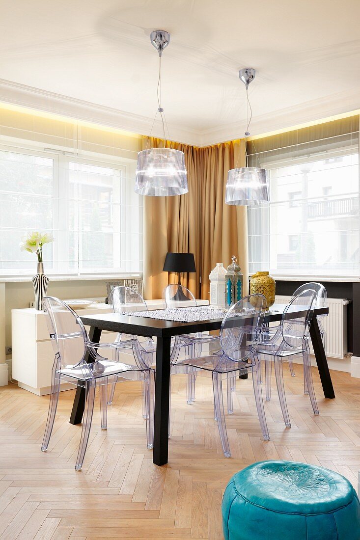 Plastic chairs around dark table below pendant lamps with transparent lampshades in dining room