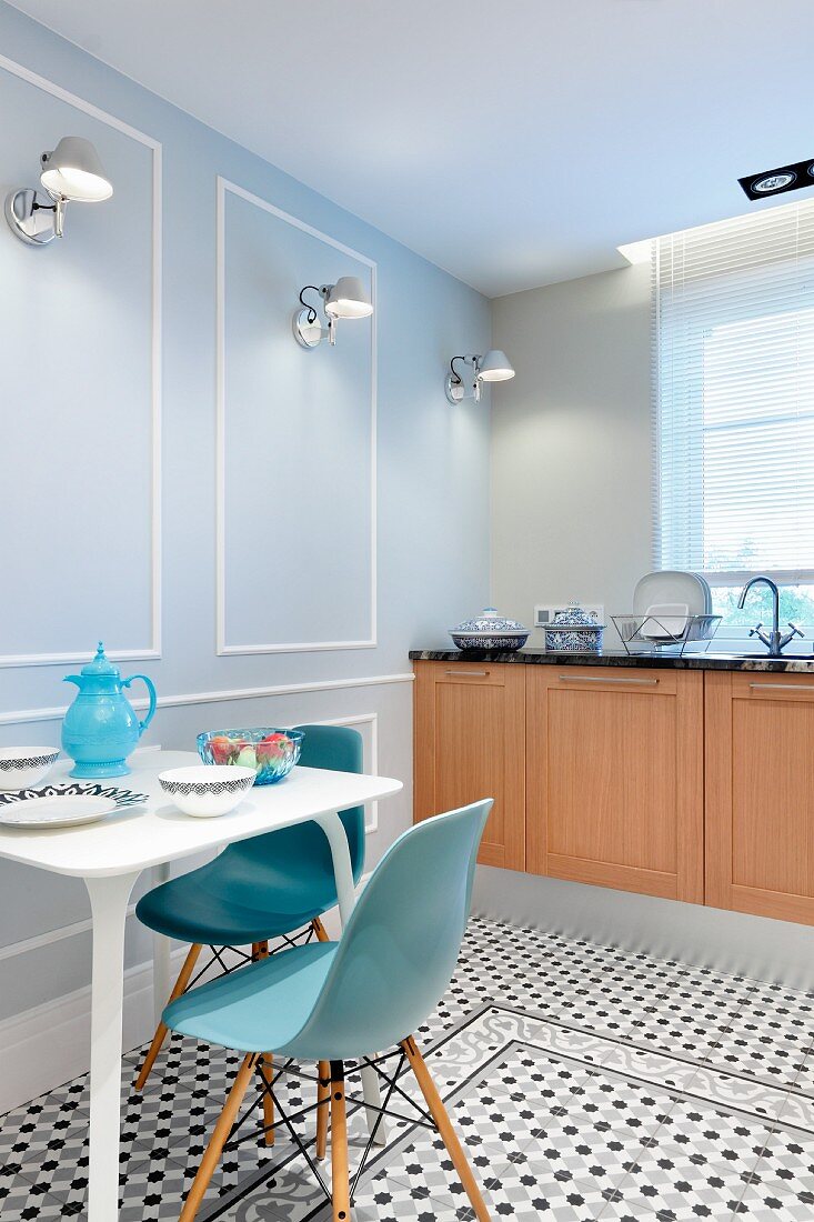 Klassikerstühle mit blauer Sitzschale an Frühstückstisch, vor Wand mit Tolomeo Wandleuchten in gerahmten Feldern, in Küche mit gemustertem Fliesenboden
