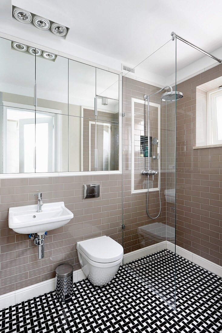 Designer bathroom with flush-fitting, mirrored cabinet, floor-level shower with glass partition and geometric, tiled floor