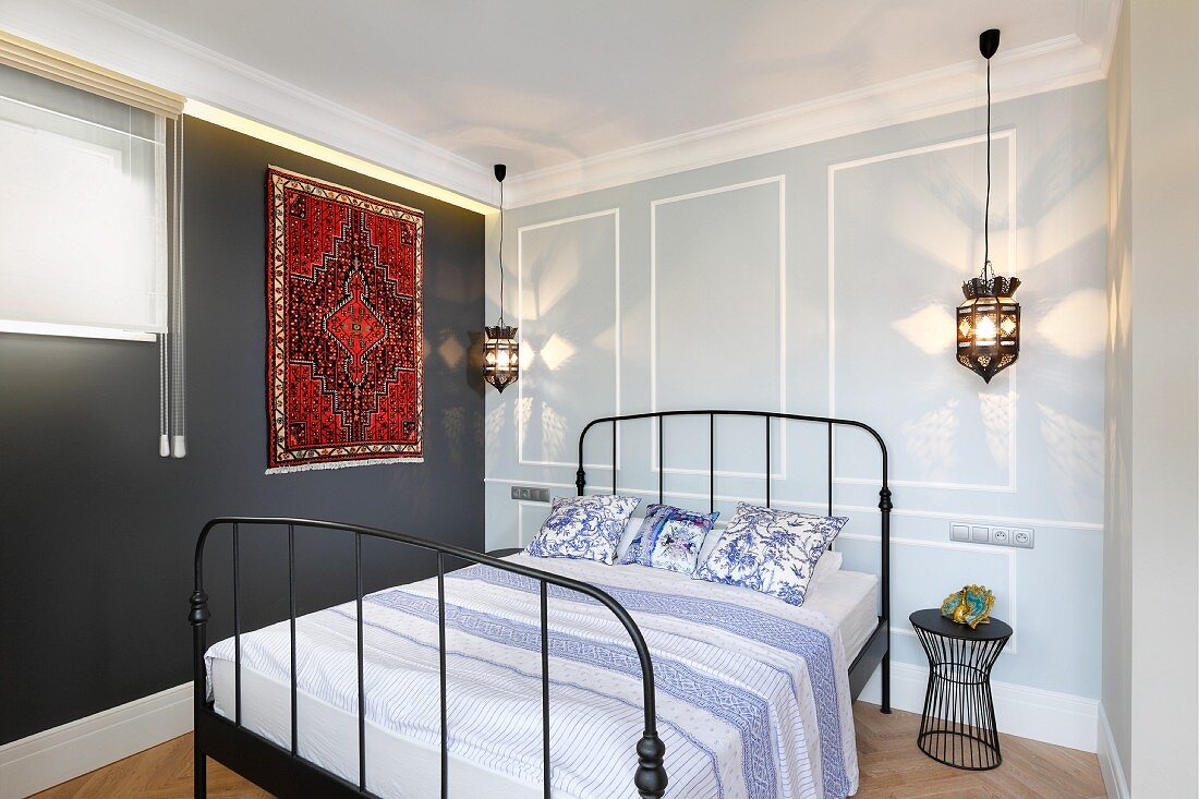 Double bed with black, metal lattice frame, Moroccan-style rug on dark grey wall and pendant lamp in bedroom