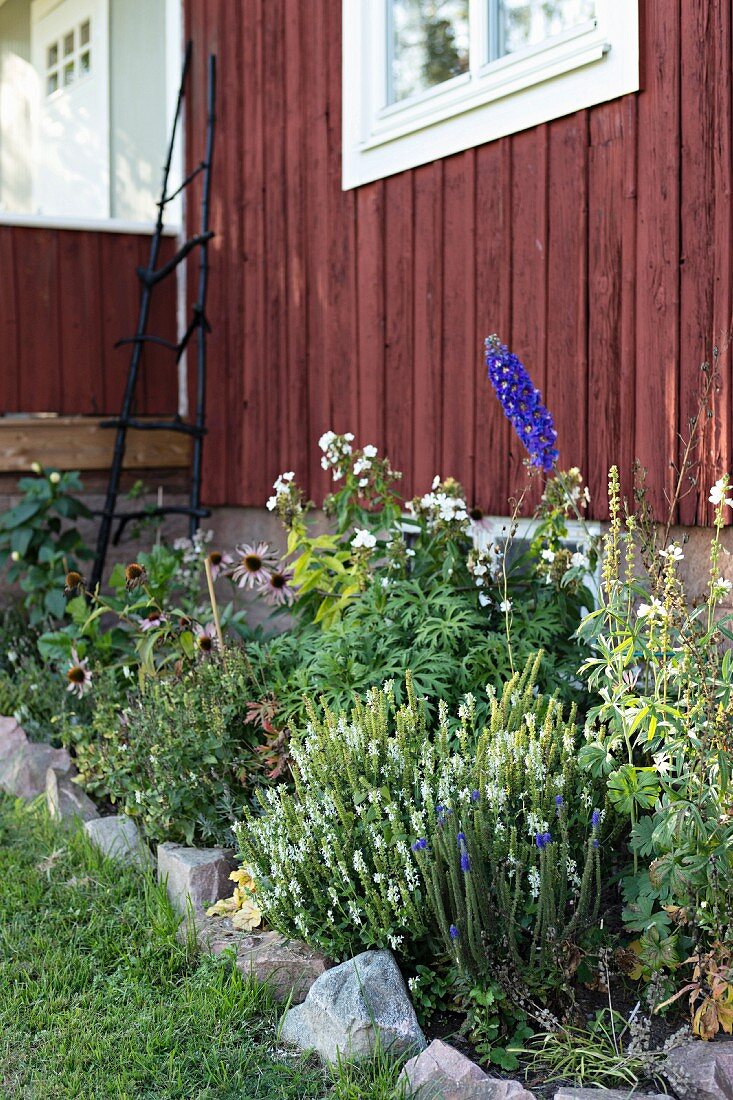 Blumenbeet mit Steineinfassung vor Holzhaus, rotbraun gestrichen