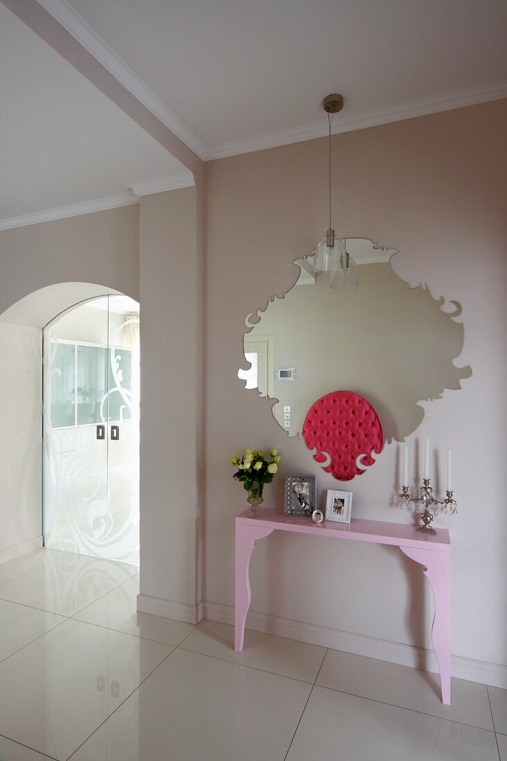 Pale pink console table below modern mirror and glass sliding doors in elegant hallway