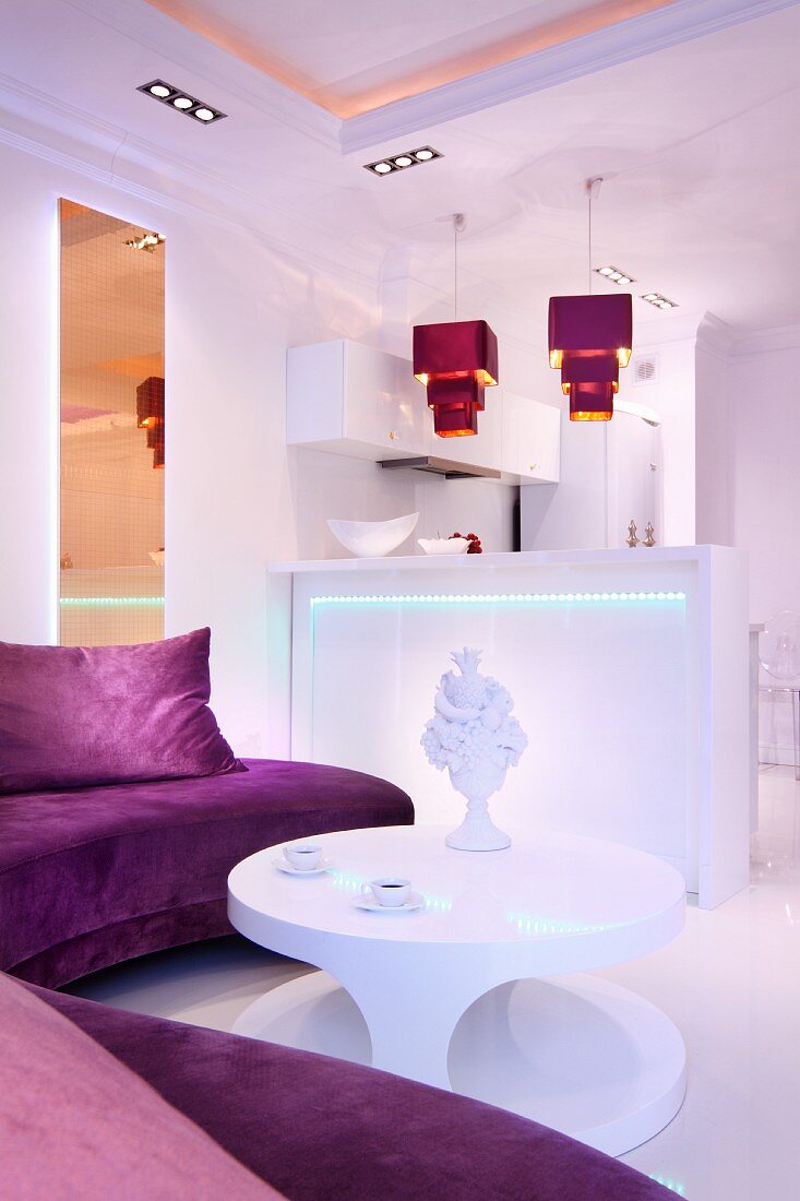 Stimmungsvoll beleuchtete weiße Küchentheke mit violettfarbenen Pendelleuchten in offenem elegantem Wohnbereich