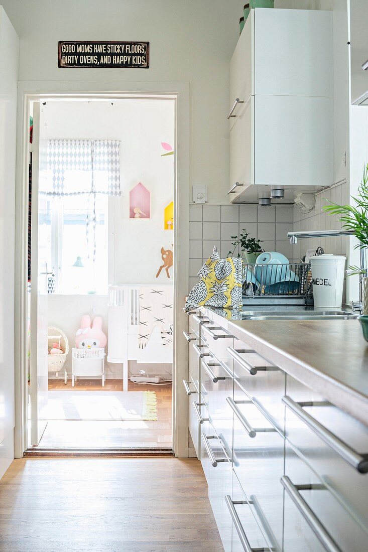 Schubladenfront einer Küchenzeile mit weissen Oberflächen; Blick durch offene Tür ins Kinderzimmer